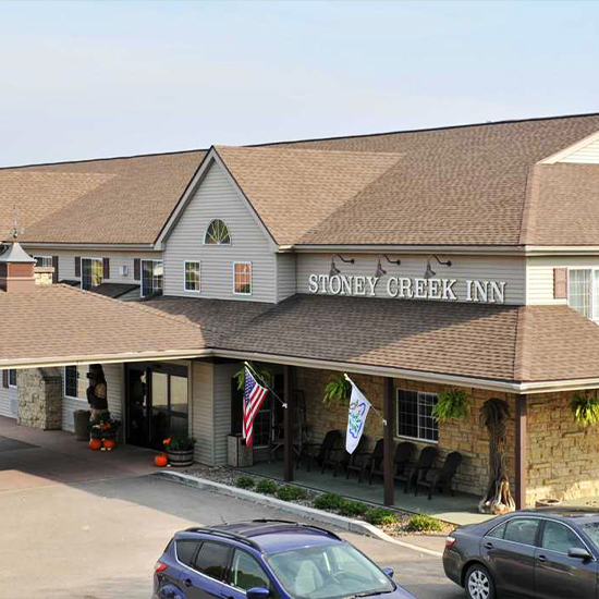 Front facade of the stoney creek hotel in galena IL. Brown roof, covered front entry, beige exterior with 2 cars in the front.